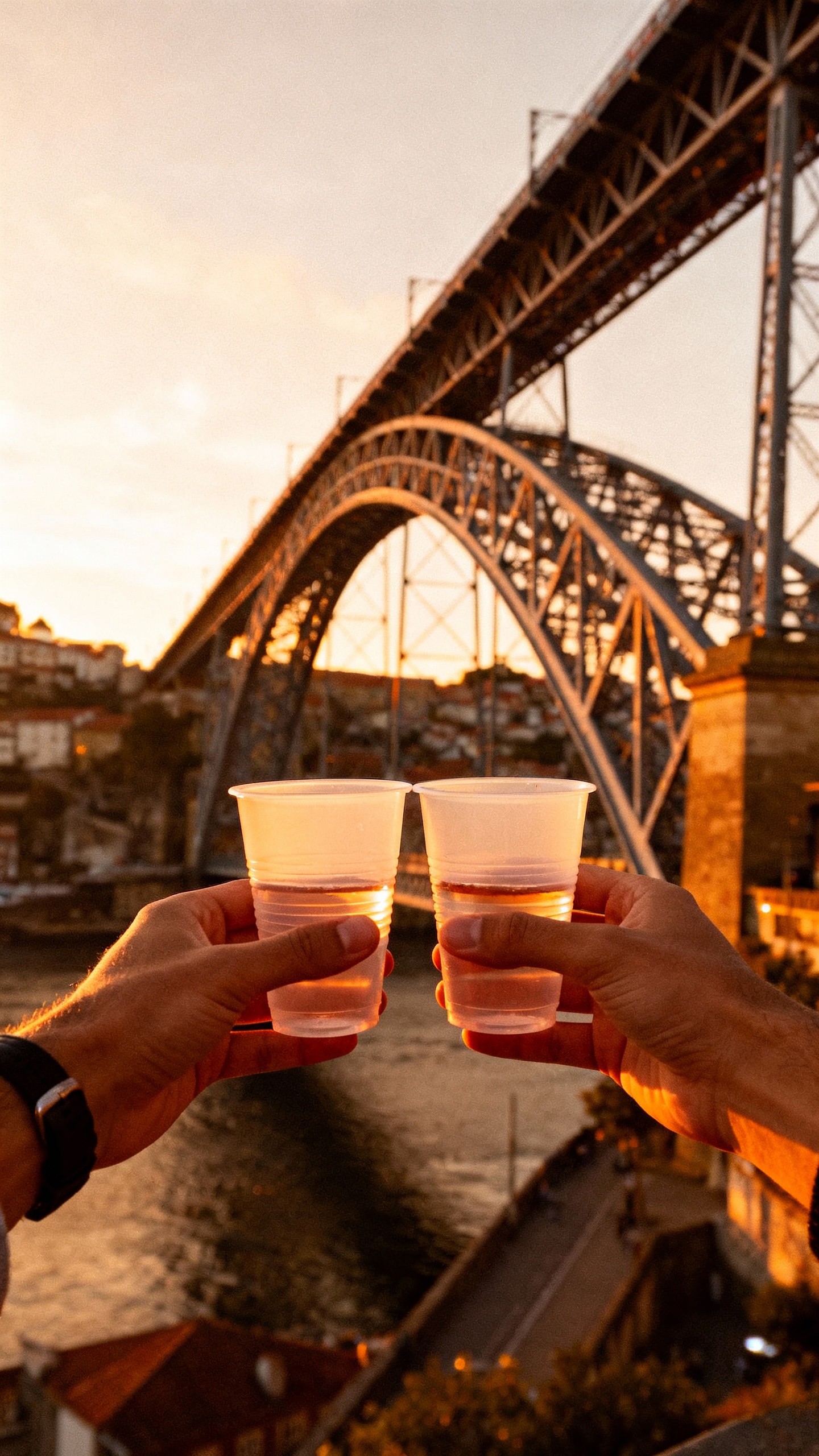 Sunset view from Dom Luís I Bridge, couple’s hands holding cheap wine plastic cups