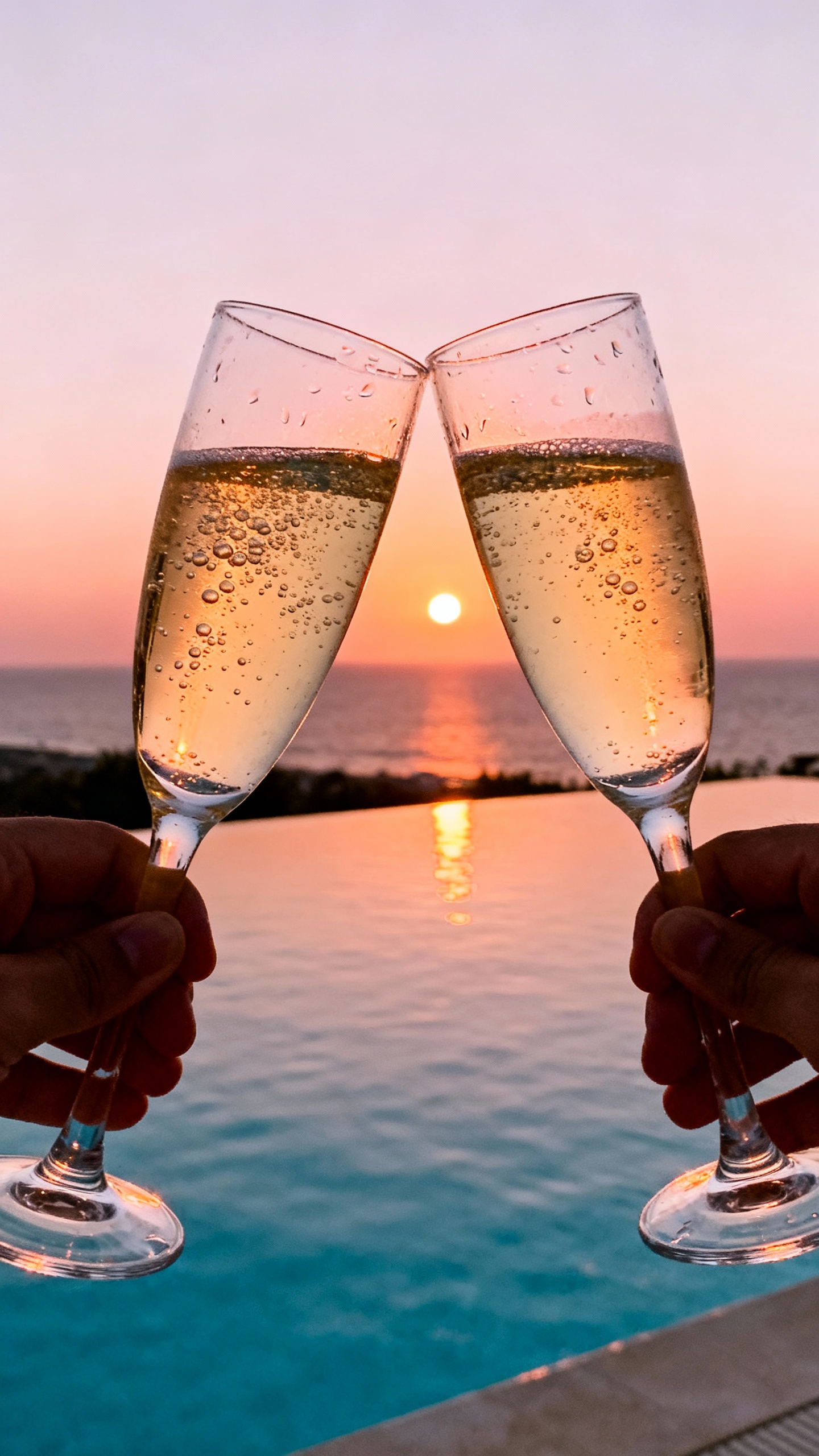 Closeup of champagne flutes clinking at sunset, ocean infinity pool reflections