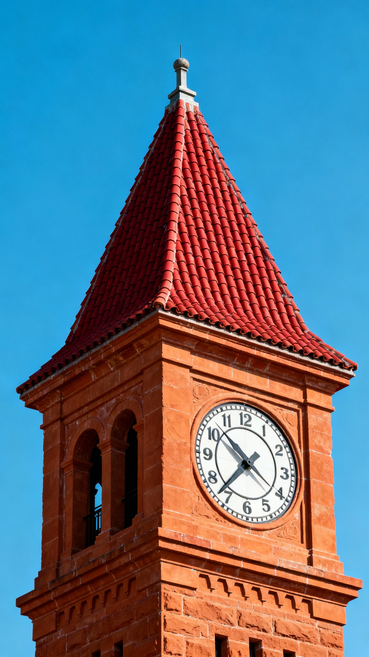 Closeup of red-tiled courthouse tower clock face, terracotta texture, blue sky